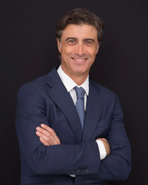 Foto profesional del Dr. Leopoldo Navarro, cirujano plástico, con traje azul marino y corbata sobre fondo oscuro