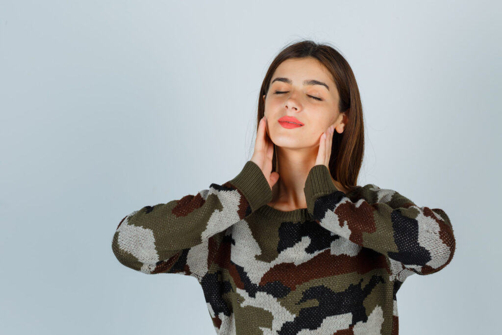Mujer joven con expresión serena tocándose el cuello y la mandíbula, transmitiendo confianza y bienestar tras una cirugía facial